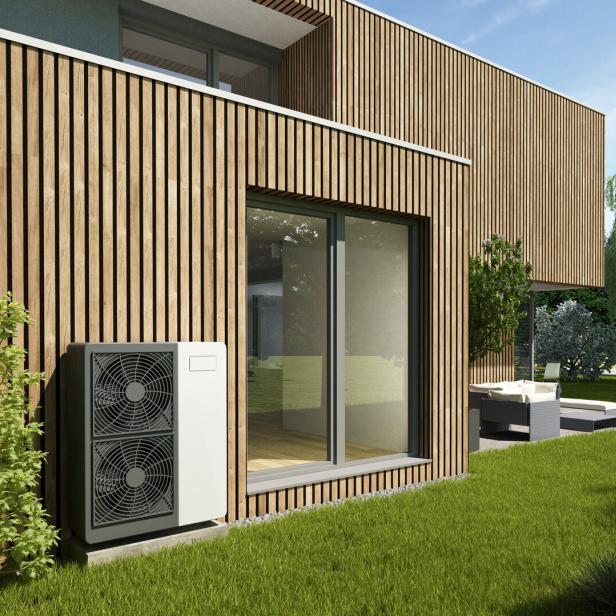 Ein modernes Haus mit Holzfassade, Wärmepumpe und großem Fenster zum Garten.