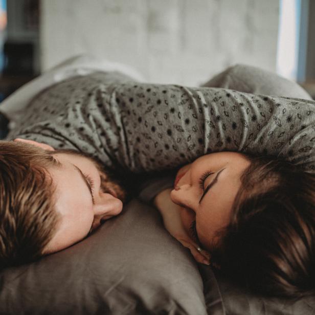 Zwei Menschen liegen eng umarmt auf einem Kissen und schlafen mit geschlossenen Augen nebeneinander.