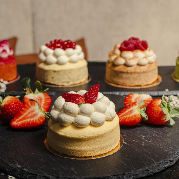 Kleine Törtchen mit Früchten und Creme stehen auf einer dunklen Platte.