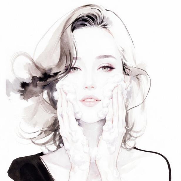 Eine Frau mit schulterlangem Haar wäscht ihr Gesicht mit Schaum und trägt ein schwarzes Oberteil.