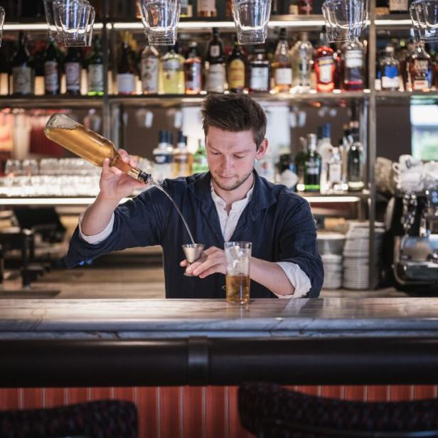 Ein Barkeeper gießt eine Flüssigkeit aus einer Flasche in einen Messbecher an einer Bar.