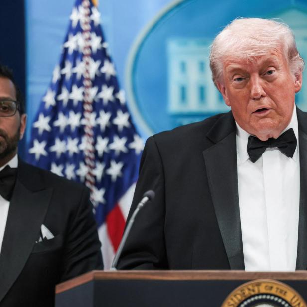 Donald Trump spricht in Anzug und Fliege vor der US-Flagge.