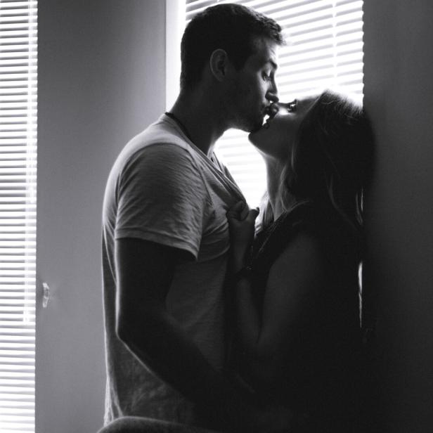 Ein Paar küsst sich leidenschaftlich vor einem Fenster mit Jalousien.