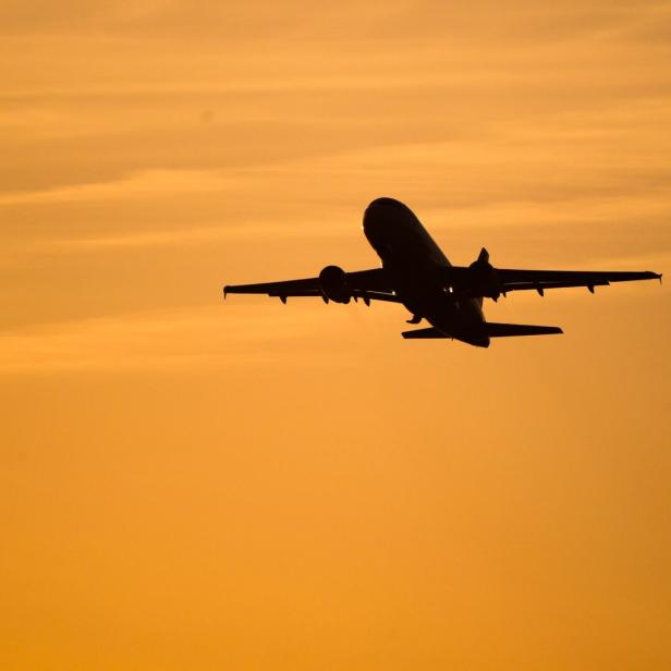 Ein Flugzeug hebt vor orangefarbenem Himmel bei Sonnenuntergang ab.