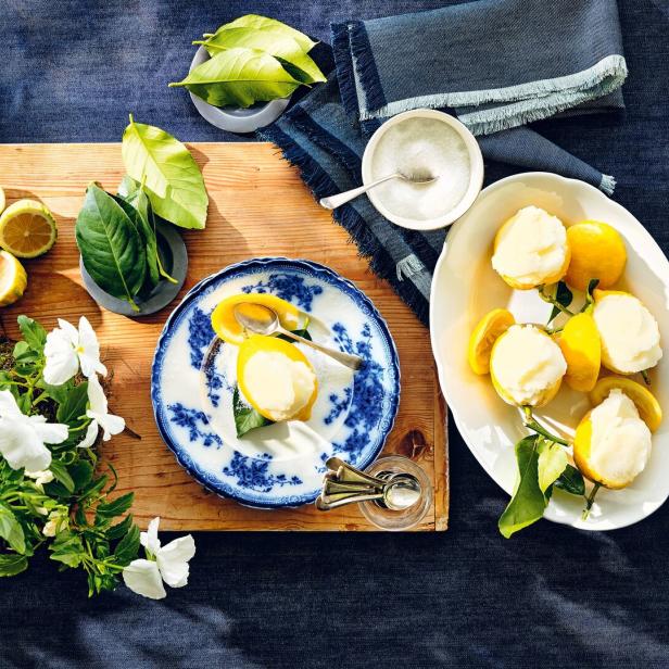 Zitronensorbet wird in ausgehöhlten Zitronenhälften serviert, daneben frische Zitronen, Blätter und weiße Blumen.