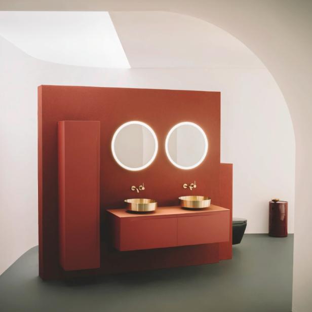 Modernes Badezimmer mit rotbrauner Wand, zwei runden Spiegeln und goldenen Waschbecken.