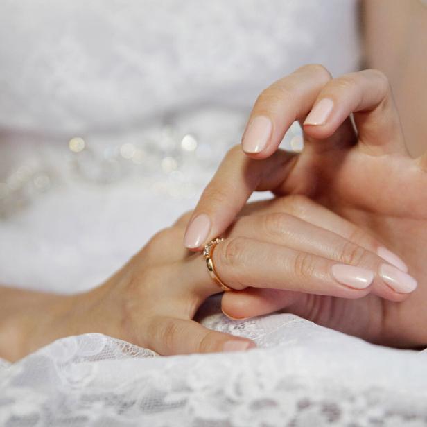 Eine Frau in weißer Spitze steckt sich einen goldenen Ring mit Stein an den Finger.