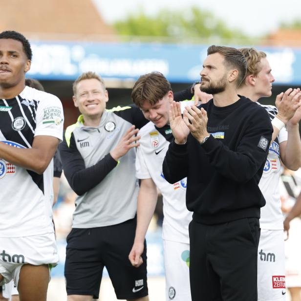 Eine Gruppe von SK Sturm Graz Spielern und Trainern applaudiert auf dem Rasen.