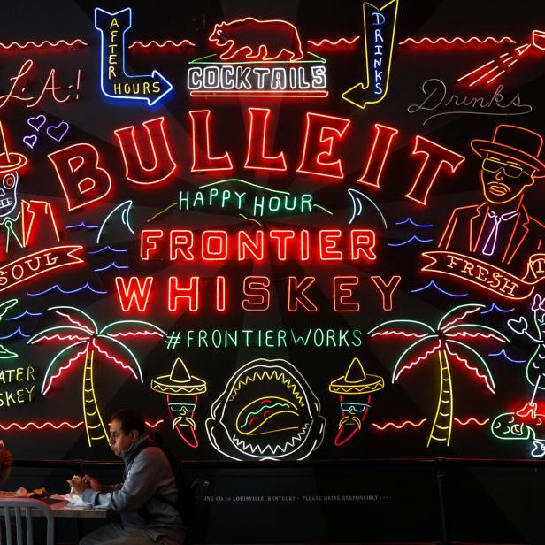 People eat in front of a sign for Bulleit Frontier Whiskey in Grand Central Market in Los Angeles