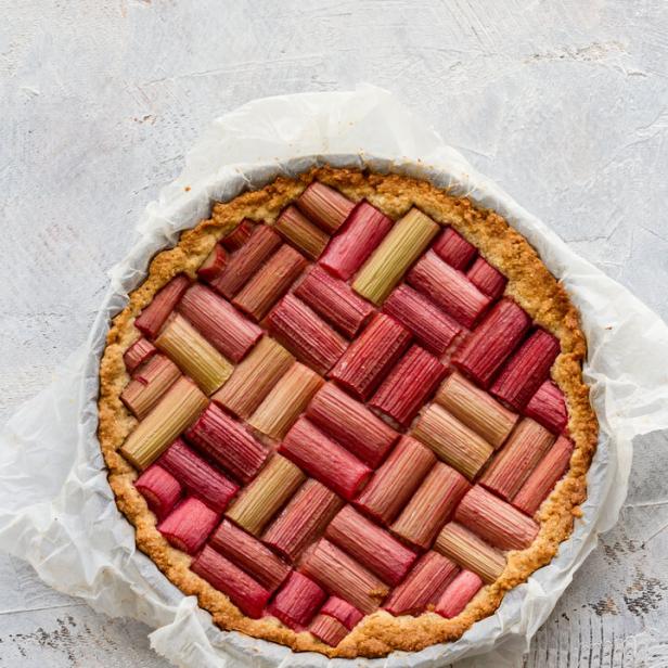 Rhabarberkuchen mit geflochtenem Muster aus verschiedenfarbigen Rhabarberstücken auf Backpapier.