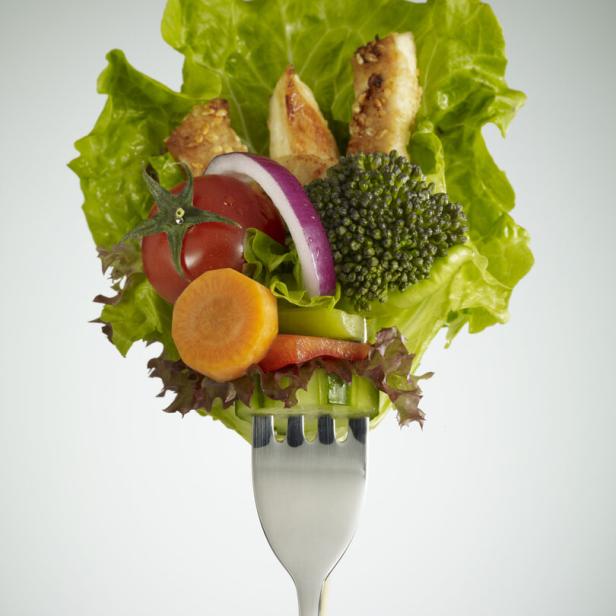 Verschiedene Gemüsestücke, Salat und Hähnchenstreifen sind auf einer Gabel aufgespießt.