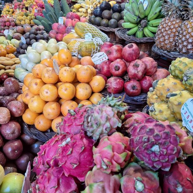 Auf einem Marktstand türmen sich exotische Früchte wie Drachenfrucht, Ananas, Bananen und Orangen.