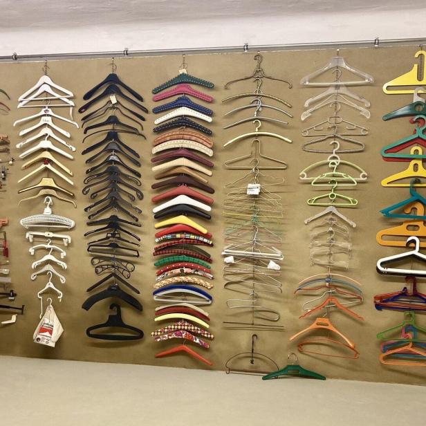 Viele verschiedene Kleiderbügel aus Holz, Kunststoff und Metall sind ordentlich an einer Wand angeordnet.