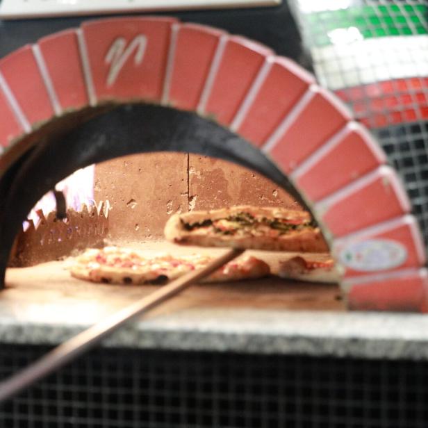 Zwei Pizzen werden mit einer Schaufel in einem traditionellen Steinofen gebacken.